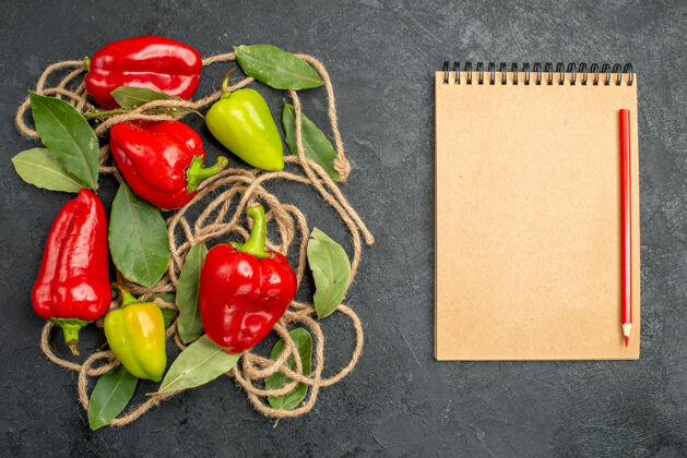 西红柿顶视图明亮的辣椒与月桂叶旁边的笔记本红笔灰色背景与自由空间胡椒健康胡椒