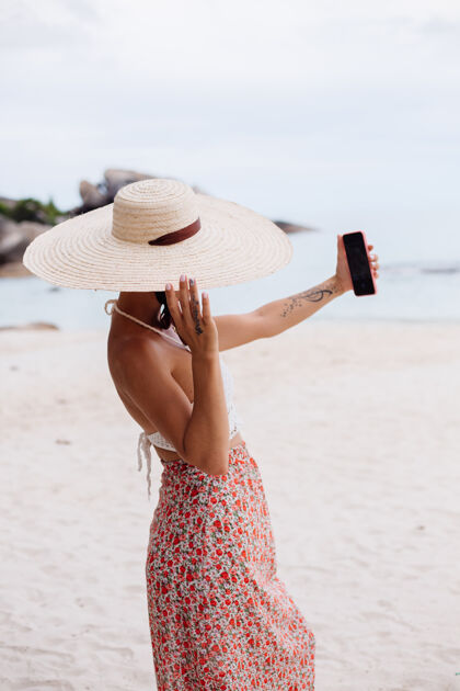 野餐沙滩上的浪漫女人穿着裙子 针织上衣 头戴草帽夏天优雅海边