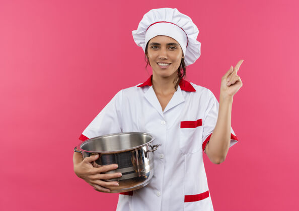 厨师面带微笑的年轻女厨师穿着厨师制服-拿着平底锅和锅盖指向旁边的复印空间盖子平底锅女