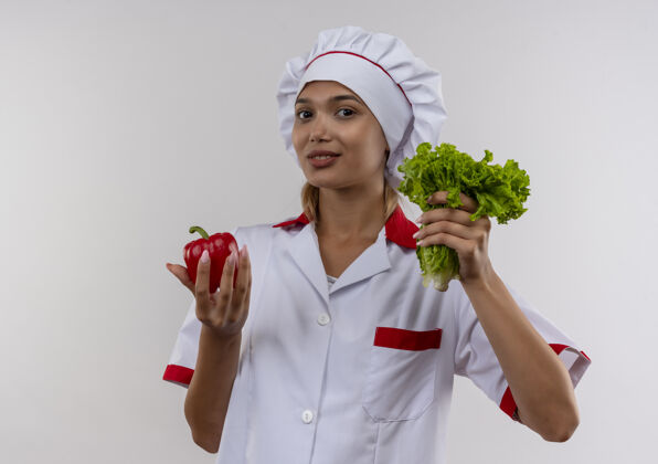 制服高兴的年轻厨师女穿着厨师制服拿着色拉和胡椒在孤立的白墙上高兴年轻胡椒粉