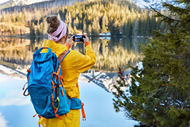 水活动女性游客照片的后视图显示 她在智能手机设备上带着山脉逃跑设备自然享受