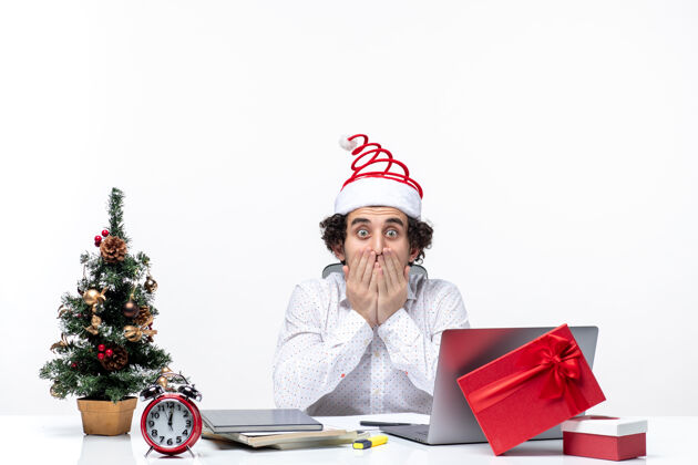电脑紧张震惊的年轻商人与有趣的圣诞老人帽子庆祝圣诞节在白色背景的办公室帽子办公室笔记本电脑
