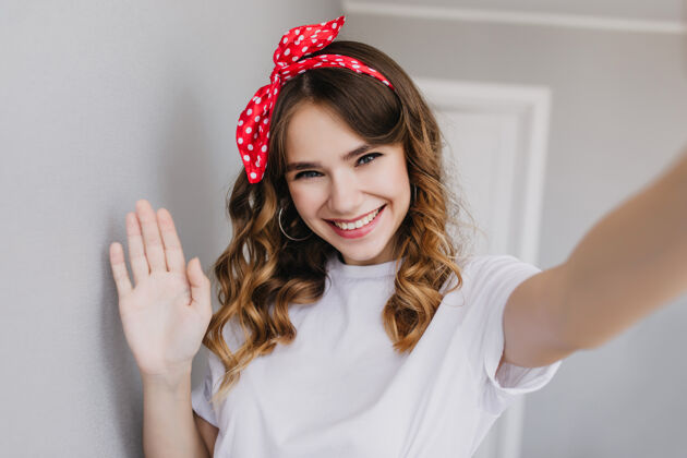 房子热情的白发女孩在家里为自己拍照快乐的女模特戴着红丝带在室内自拍卷发快乐人