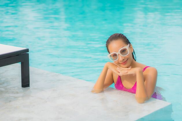 放松肖像美丽的亚洲年轻女子放松微笑周围的室外游泳池在酒店度假村身体帽子泳装