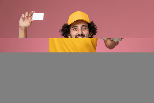 服务正面图：身穿黄色制服的男信使手拿棕色的咖啡杯和浅粉色墙上的白色卡片棕色黄色手持