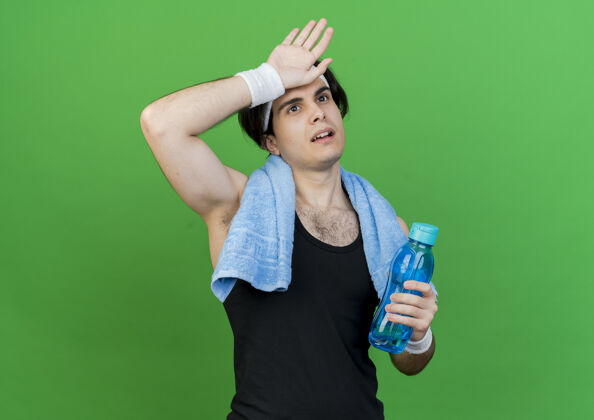 年轻一个穿着运动服 头戴头巾 脖子上围着毛巾 手里拿着一瓶水的年轻人看起来很疲倦 精疲力竭运动装看头带