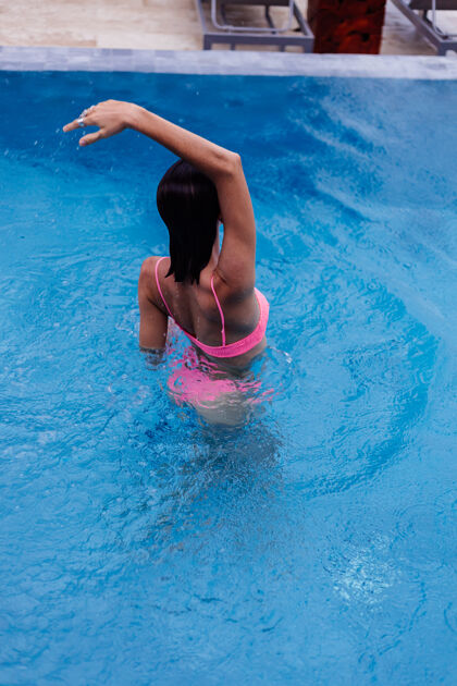 快乐在明亮的粉红色比基尼蓝色游泳池里的年轻快乐修长的欧洲女人女人泳装海滩