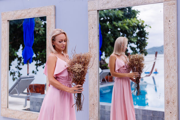 豪华浪漫写真的粉红色晚装可爱的女人手持野花在豪华热带别墅外美丽的女性与花束享受优雅女人