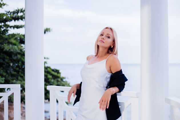 冷静时尚写真时尚的白种女人在丝绸长裙黑色外套豪华的地方与海景黑色魅力优雅