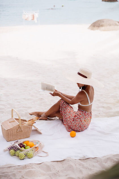 肖像一个年轻女子戴着草帽 穿着白色针织衣服坐在沙滩地毯上奢华天堂白色
