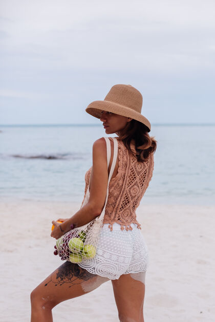 快乐年轻漂亮的白种人 皮肤黝黑 穿着针织衣服 戴着帽子在沙滩上度假女性棕色