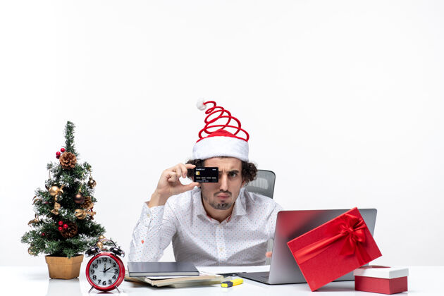 帽子在白色背景的办公室里 戴着圣诞老人帽 出示银行卡的年轻商务人士带着节日的喜庆心情微笑银行商务
