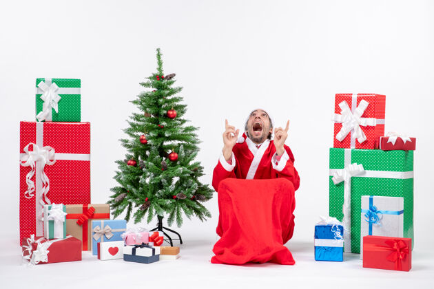 圣诞情绪激动的年轻人打扮成圣诞老人与礼物和装饰圣诞树上的白色背景圣诞老人礼物购物