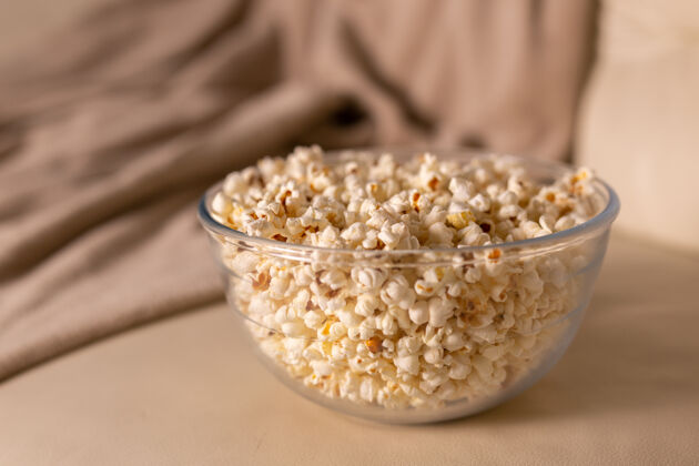 娱乐一碗爆米花在米色沙发上看电影零食和不健康的垃圾食品的概念休闲玉米室内