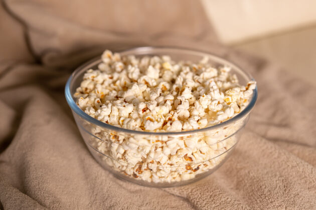 娱乐一碗爆米花在米色沙发上看电影零食和不健康的垃圾食品的概念美味电影室内